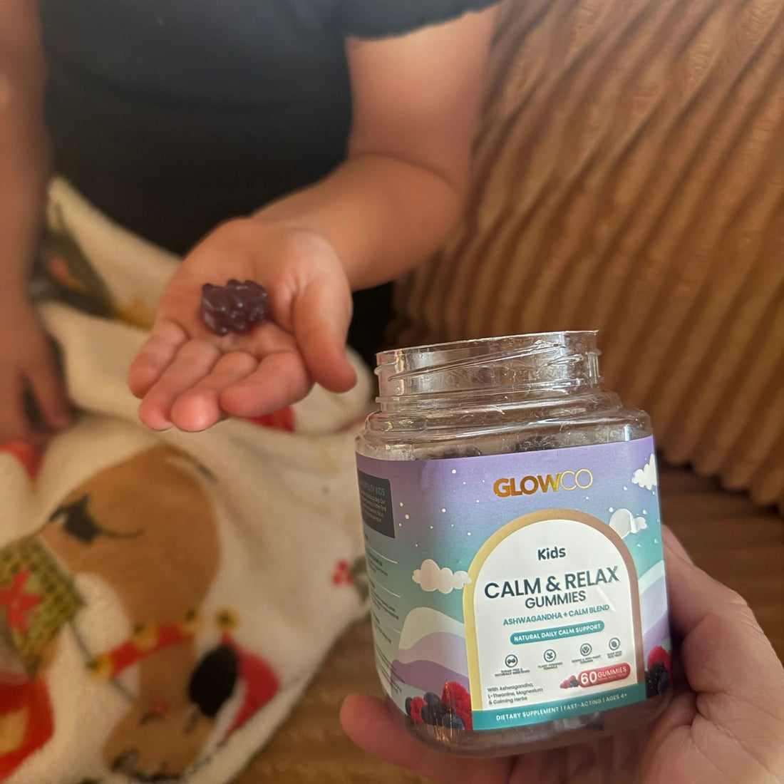 Child holding a Glowco Kids Calm & Relax gummy next to the jar