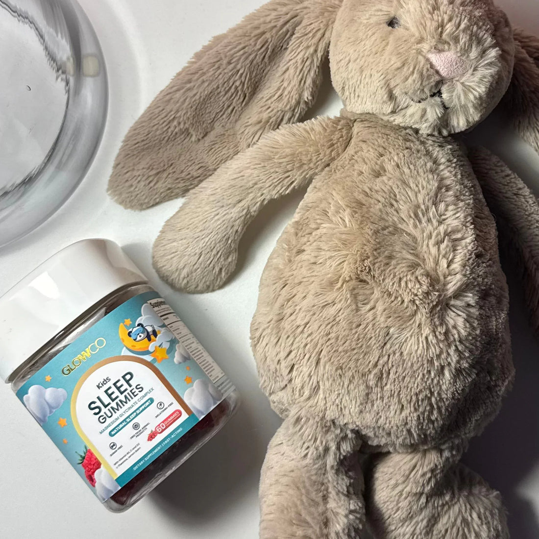 Glowco Kids Sleep Gummies jar with a soft toy bunny at bedtime